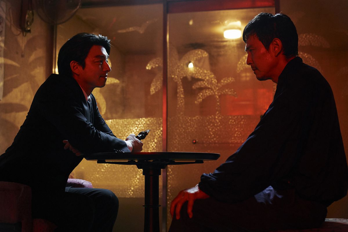 Rekryteraren och Gi-hun (spelade av Gong Yoo respektive Lee Jung-jae) sitter vid ett bord, med rekryteraren som håller vad som ser ut som en pistol riktad bort från bordet
