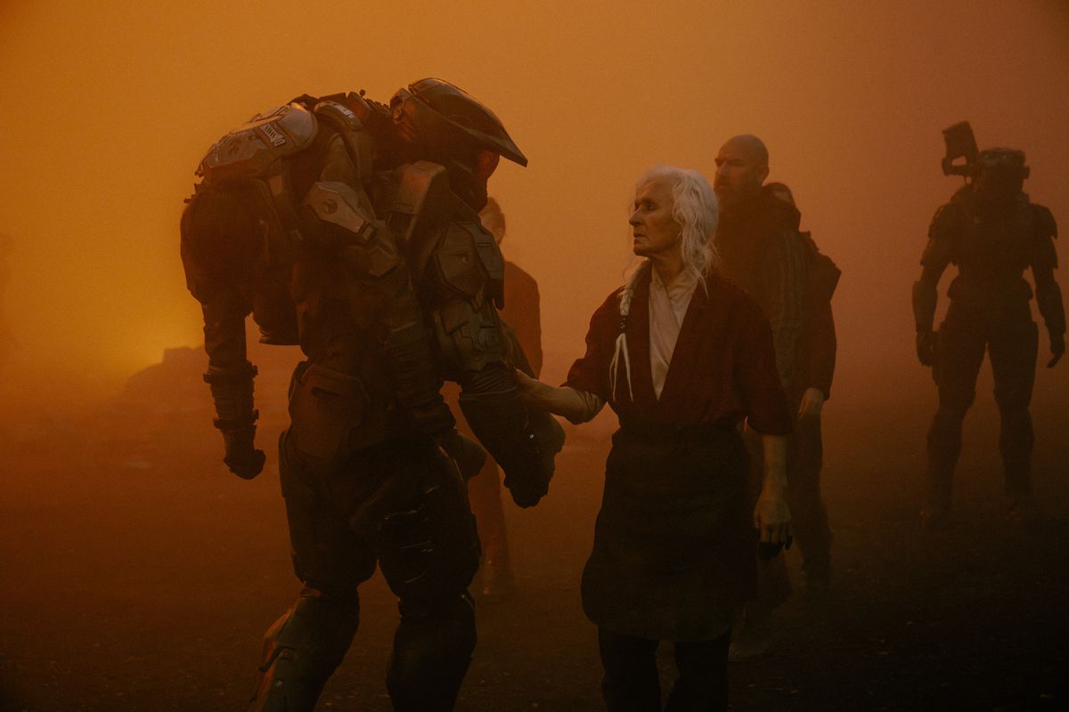 Master Chief bär en skadad marinsoldat över sin axel medan eld och aska täcker himlen i Halo säsong 2