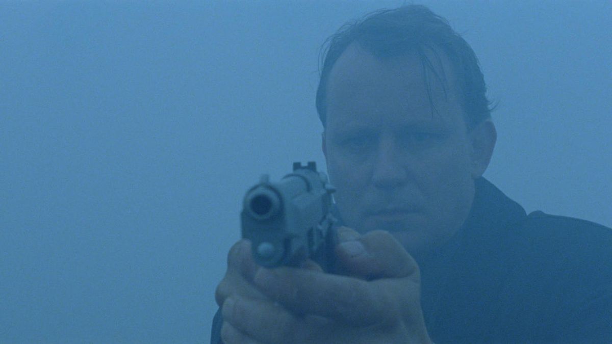 Ett mediumbild av en man som håller i en pistol omgiven av dimma.
