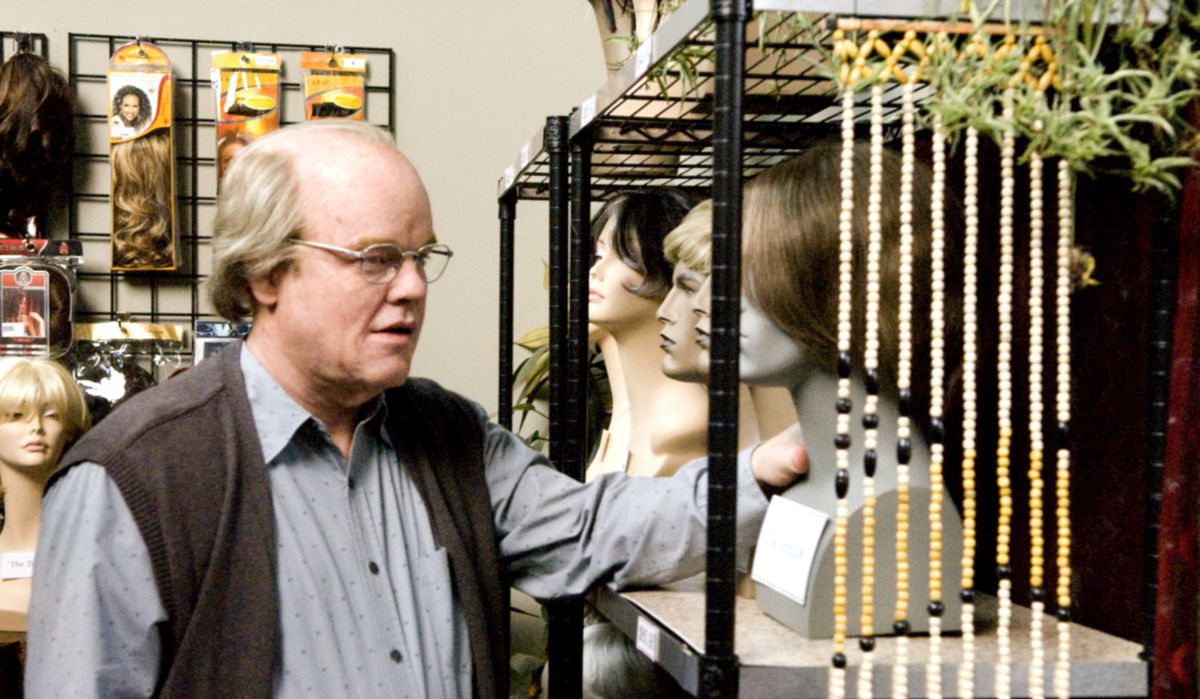 Teaterchefen Caden (Philip Seymour Hoffman), en skallig, åldrande man i glasögon, tittar på en visning av skyltdockahuvuden med peruker bakom scenen på en pjäs i Synecdoche, New York