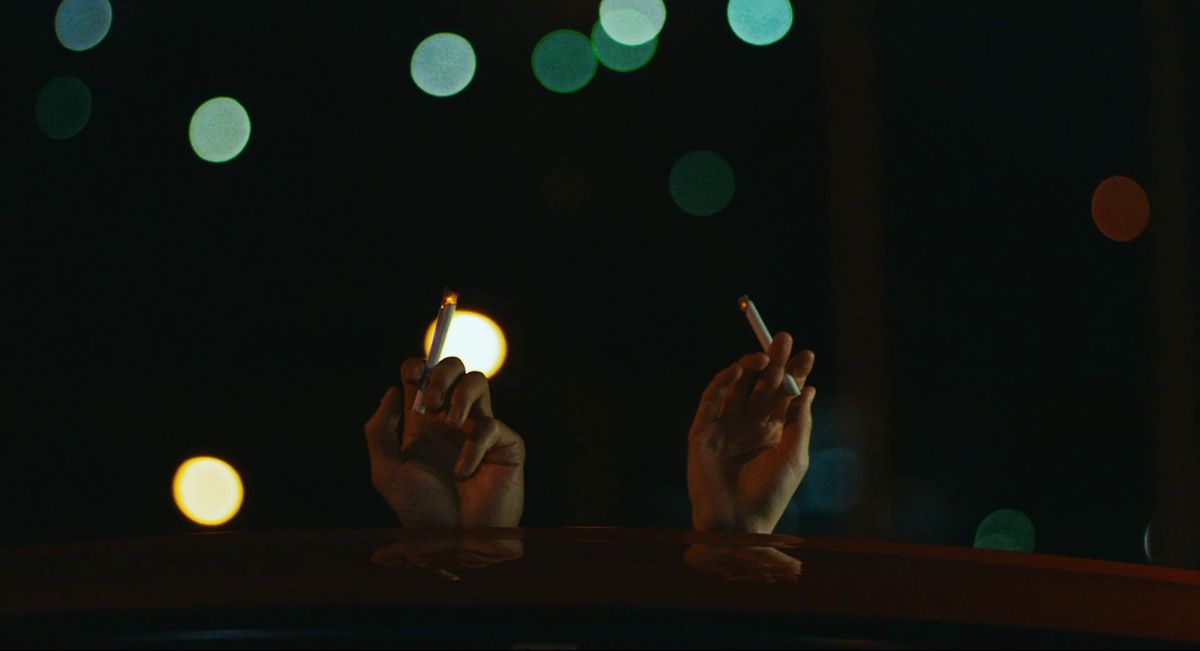 Två händer på taket av en bil som håller cigaretter mot natthimlen.