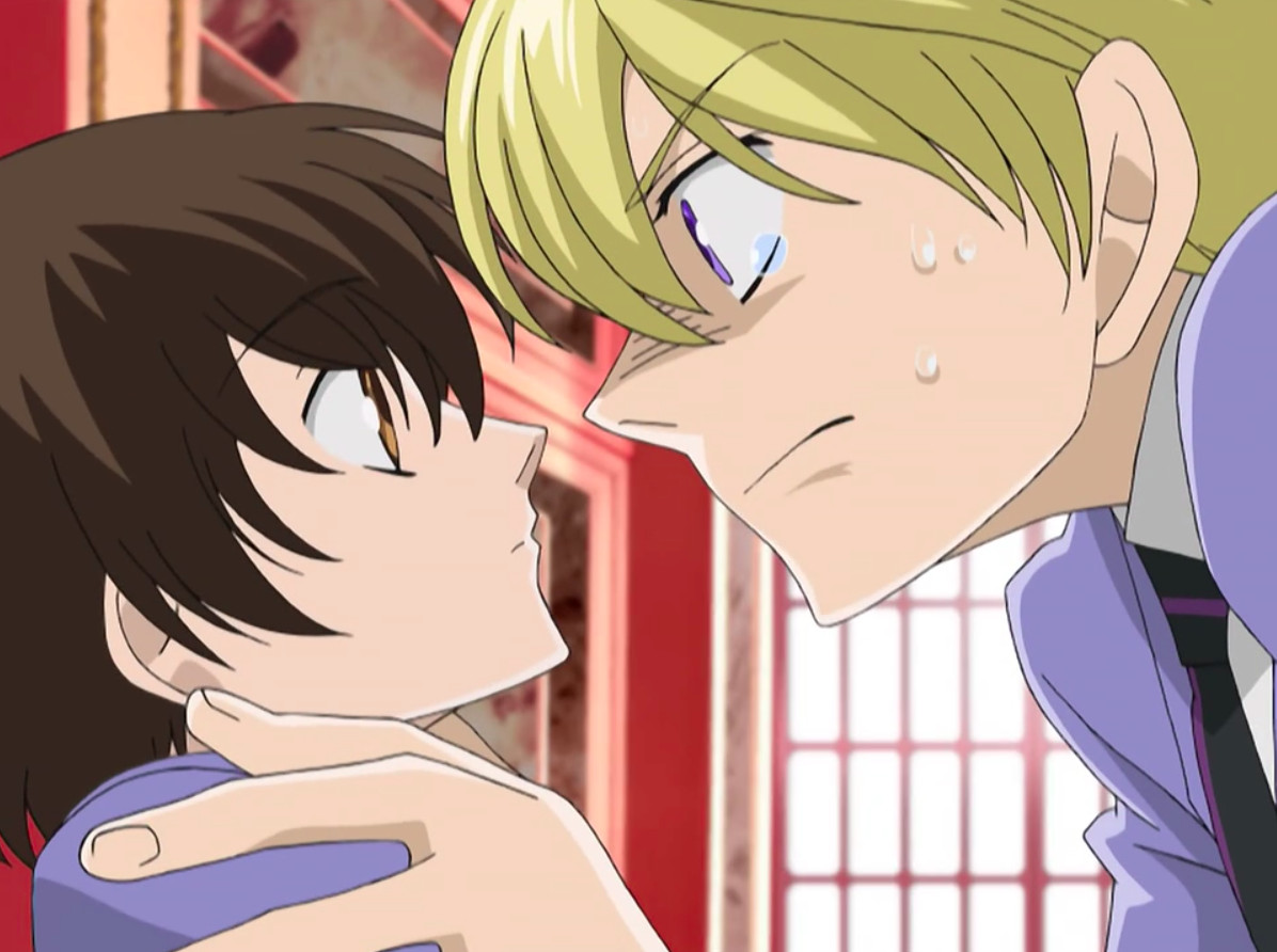 Karaktärer från Ouran High School Host Club — Tamaki, till höger, greppar Haruhi om axlarna.  Hon ser oberörd ut men tittar tillbaka upp på honom.  Hans uttryck är intensivt.