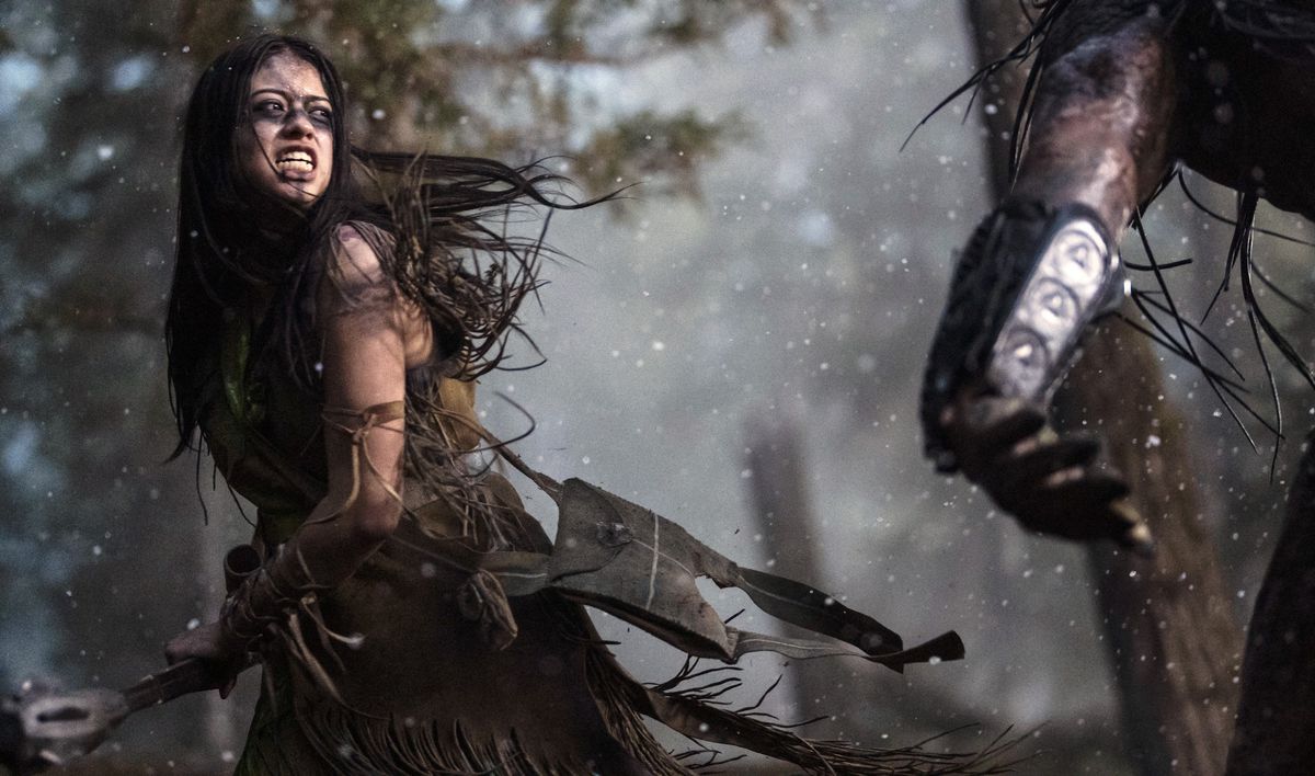 Naru (Amber Midthunder), en Comanche-kvinna i handgjorda läderkläder, blottar sina tänder i ett morrande när hon möter den annalkande Predator i Prey