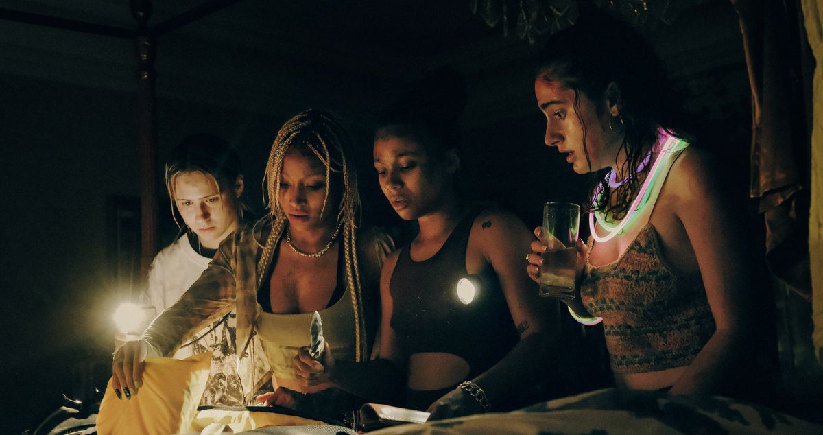 Four of the women of Bodies Bodies Bodies gather around a candle in the dark