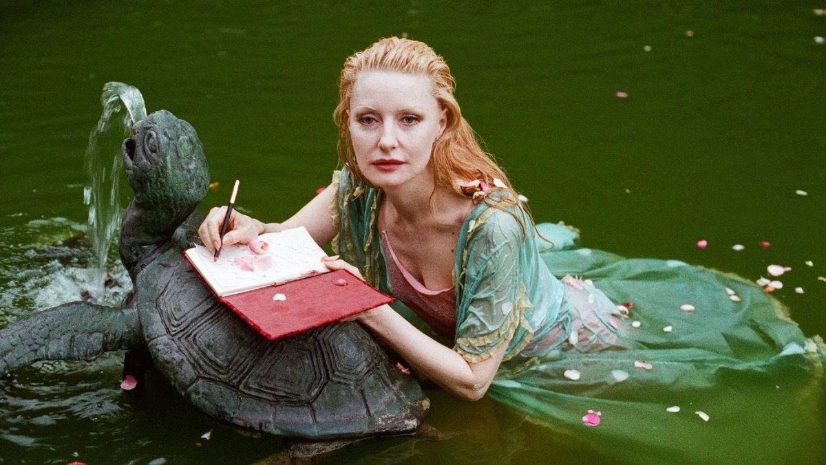 Shere Hite, iklädd en ljusgrön klänning, flyter i vattnet med en anteckningsbok öppen på en staty av en sköldpadda.  Hon ser mer än lite ut som en sjöjungfru.  Bilden är från dokumentären The Disappearance of Shere Hite