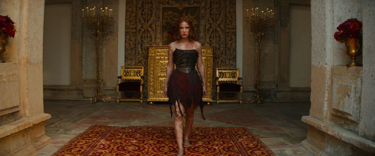 Elodie, spelad av Millie Bobby Brown, går genom de förgyllda palatsets korridorer i en förstörd, sönderriven och bränd klänning, beslutsamhet i ansiktet