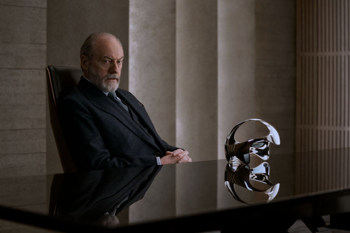 Thomas Wade (Liam Cunningham) sitter vid ett skrivbord med ett futuristiskt headset på ett bord.