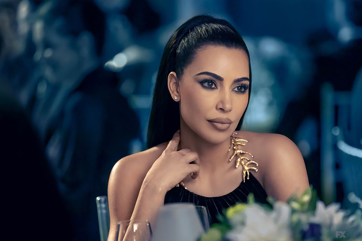 Kim Kardashian looking glamorous while seated at a table in American Horror Story: Delicate