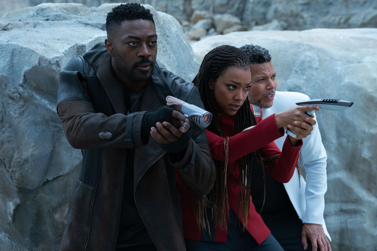 David Ajala and Sonequa Martin-Green hold up Star Trek phasers, standing next to Wilson Cruz on a rocky planet in Star Trek: Discovery