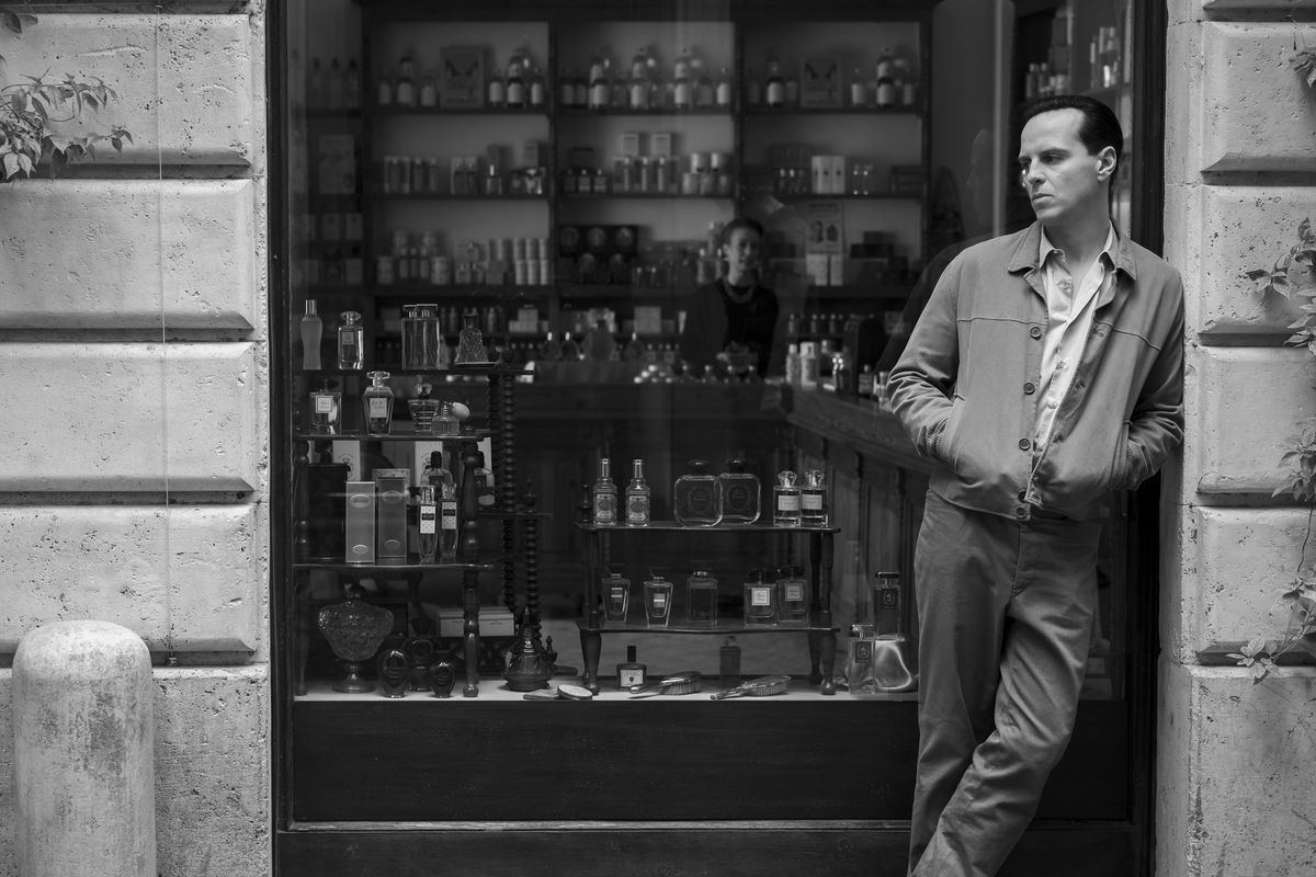 In a black-and-white image from Ripley, Andrew Scott leans against a wall in front of a store window that has lots of liquor bottles in it. He looks kinda sad but in a hot way.