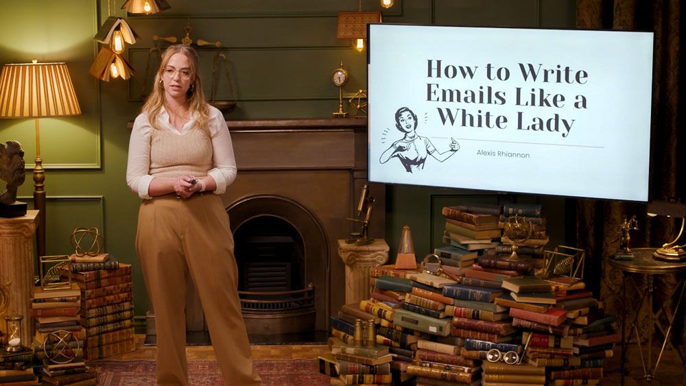 Alexis Rhiannon, stands on an academically decorated living room set next to a big screen TV displaying the title “How to Write Emails Like a White Lady,” in Dropout’s Smartypants. 