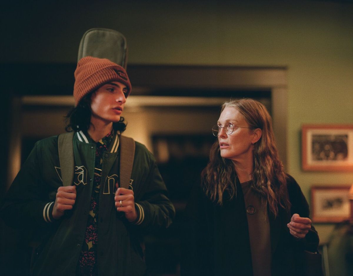En tonårspojke (Finn Wolfhard) med ett gitarrfodral på ryggen står bredvid en äldre, långhårig kvinna (Julianne Moore) med glasögon.
