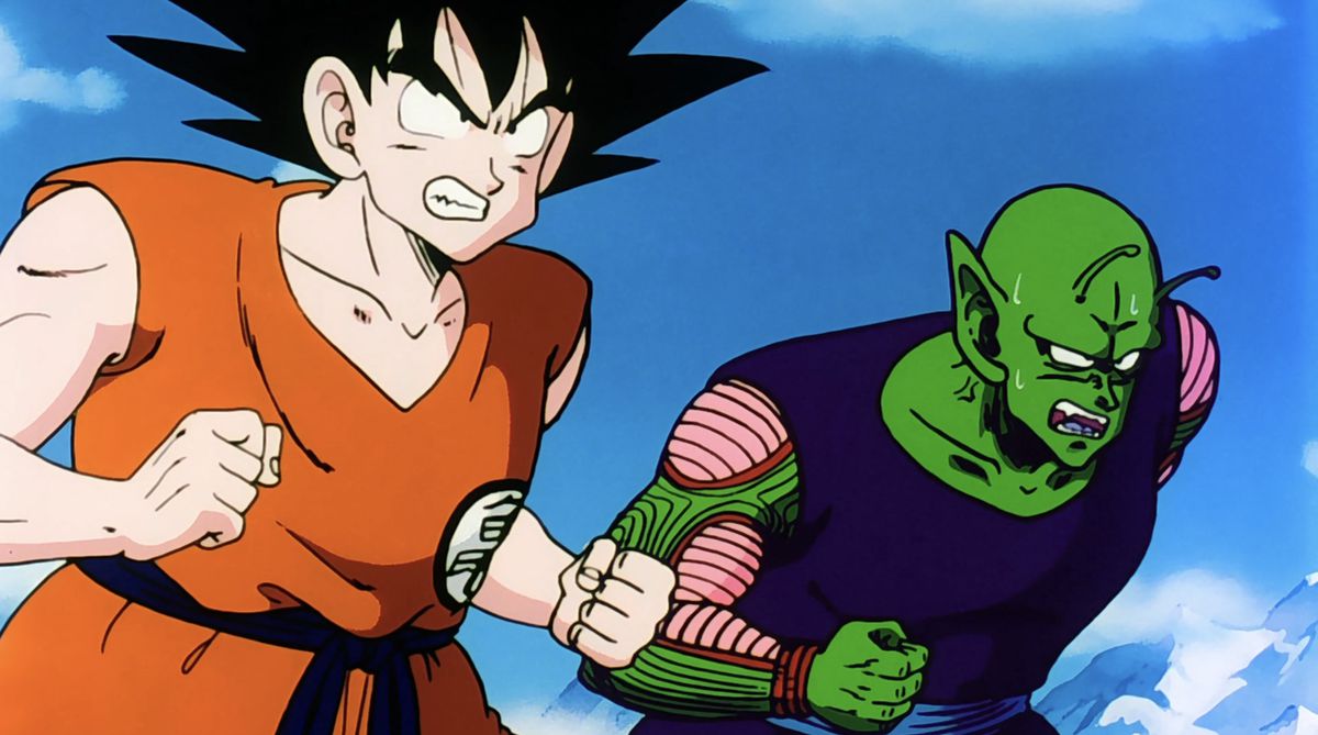 Goku och en svettig Piccolo står sida vid sida för att slåss mot en gemensam fiende, båda blottar sina tänder för att visa att de är redo att slåss i Dragon Ball Z