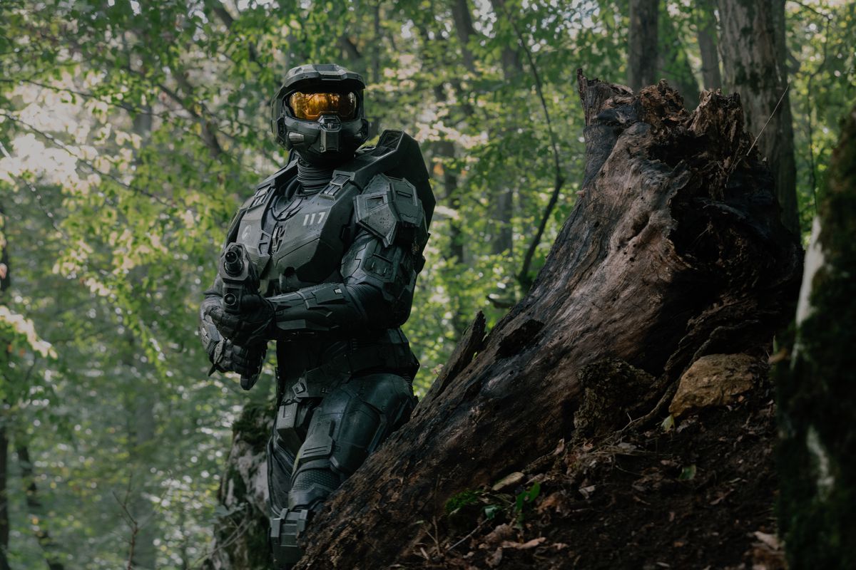 Pablo Schreiber i Master Chief-rustningen håller ett automatgevär och går genom skogen med en stubbe framför sig i Halo säsong 2