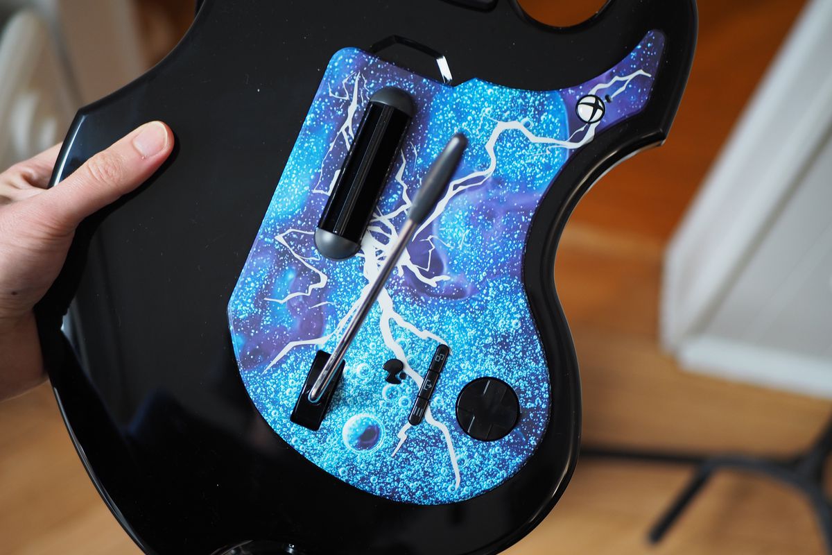 Ett foto taget av PDP Riffmaster trådlösa gitarrkontroller.  Det här fotot fokuserar på pickguard-området på gitarrkontrollern, och framhäver den abstrakta designen av den begränsade tidens pickguard, såväl som kontrollerns andra funktioner, inklusive strum bar, whammy bar, d-pad, Xbox-knapp, såväl som starten , välj och volymjusteringsknappar.