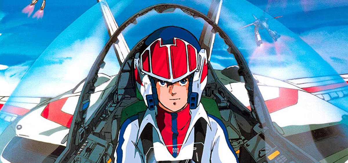 En anime man bär en röd och blå stridspilot outfit och hjälm i sittbrunnen på en transformerande robot i Super Dimension Fortress Macross.
