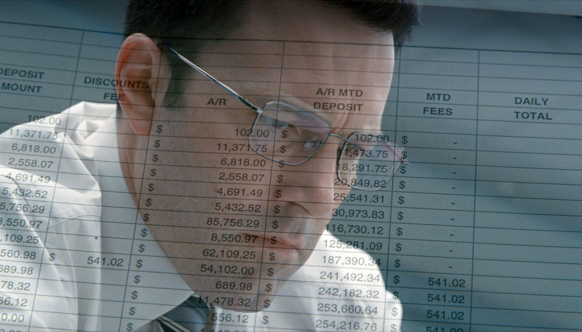 Ben Affleck tittar ner med siffror och kalkylblad på papper över hans ansikte i The Accountant 