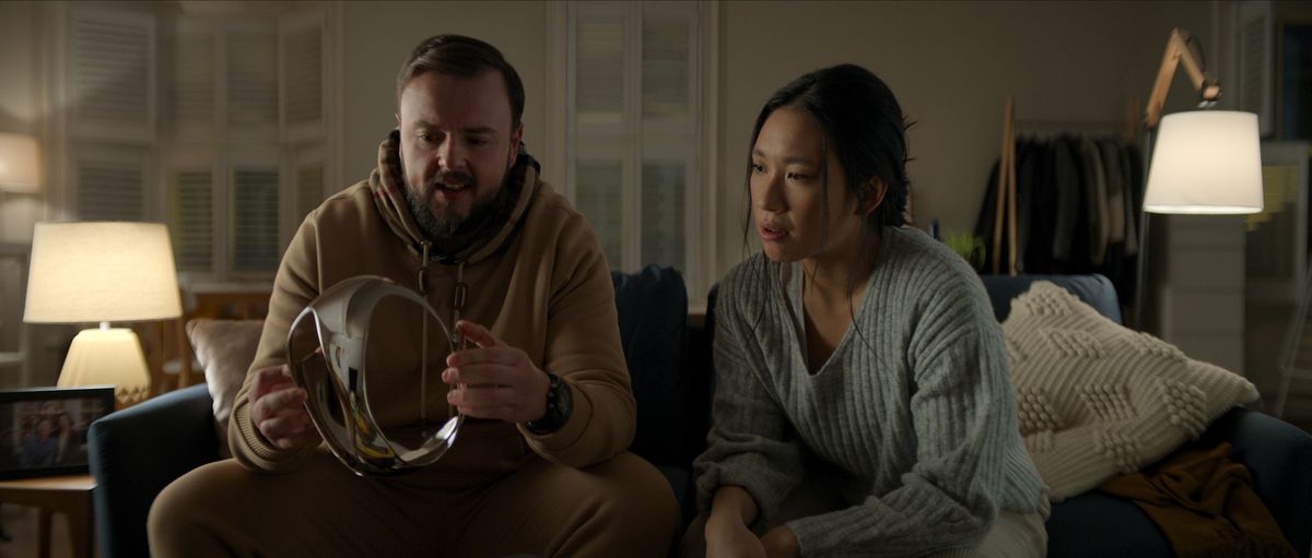 John Bradley som Jack Rooney och Jess Hong som Jin Cheng sitter på en soffa och tittar på VR-headsetet i krom i avsnitt 102 av 3 Body Problem