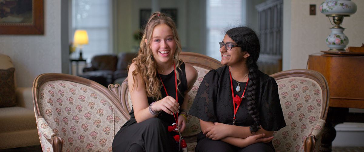 Two girls seated on a couch and smiling.