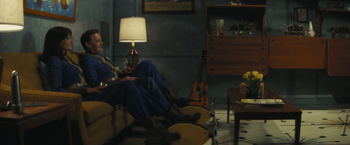 Lucy (Ella Purnell) och hennes pappa Hank (Kyle MacLachlan) sitter på en soffa och ler i ett Vault-vardagsrum