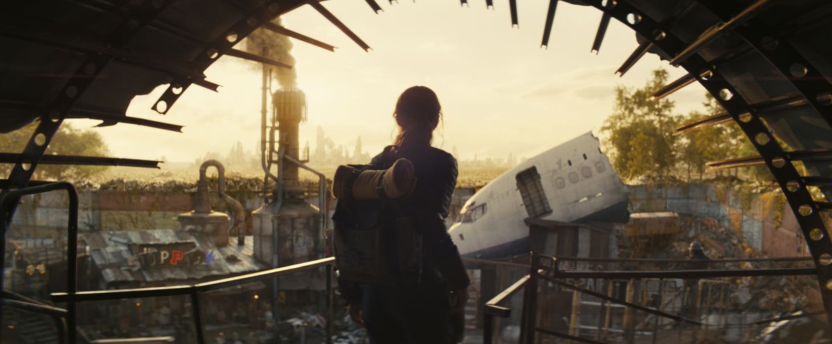 En ung kvinna med en ryggsäck som stirrar ut mot en stad gjord av rensad metall i TV-serien Fallout.