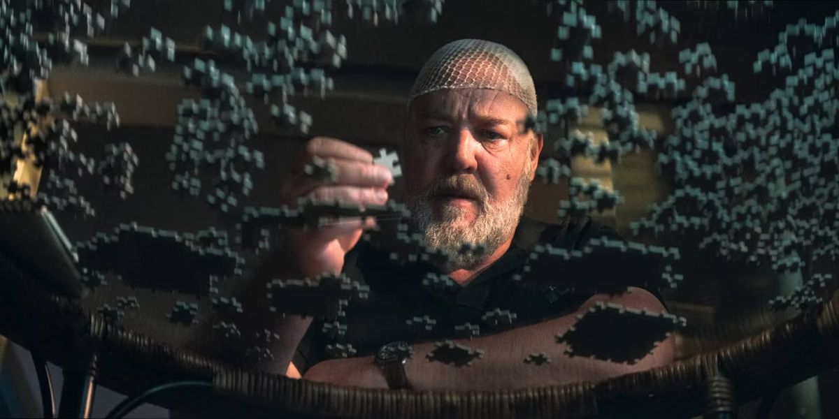 A man wearing a hairnet holding a puzzle piece while staring at a glass table of puzzle pieces.