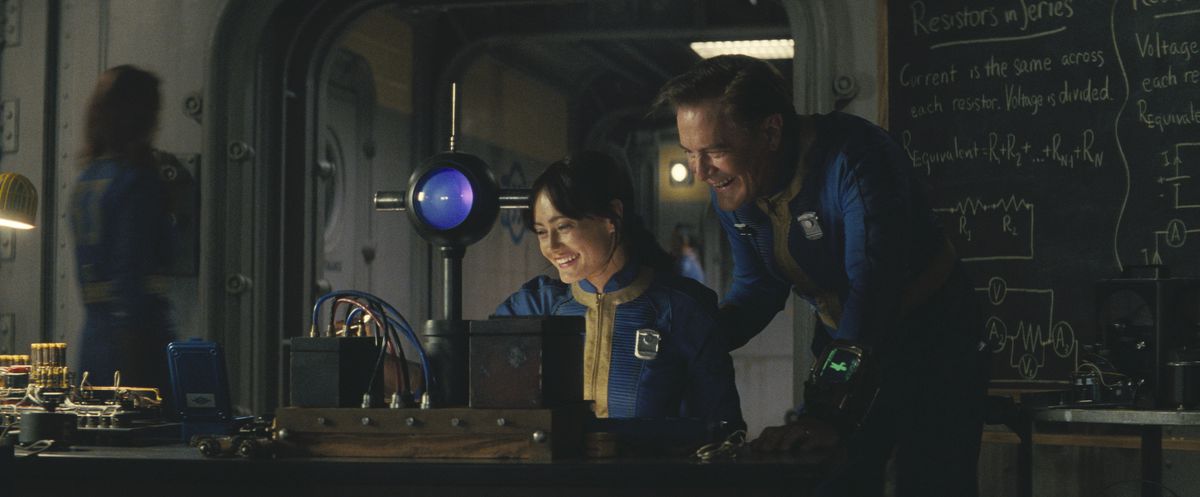 Lucy (Ella Purnell) och hennes pappa, Overseer Hank (Kyle Maclachlan) skrattar över ett vetenskapligt experiment i en stillbild från Fallout säsong 1