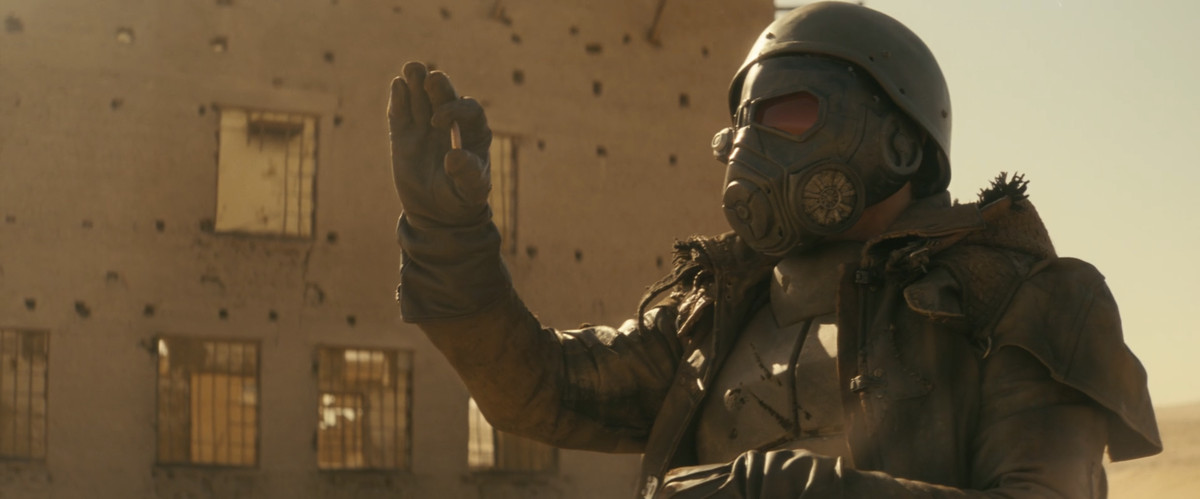 Adam the Lead Farmer (Erik Estrada) i Fallout håller upp ett kulhus och undersöker det.  Han har på sig Fallout New Vegas kurir-look