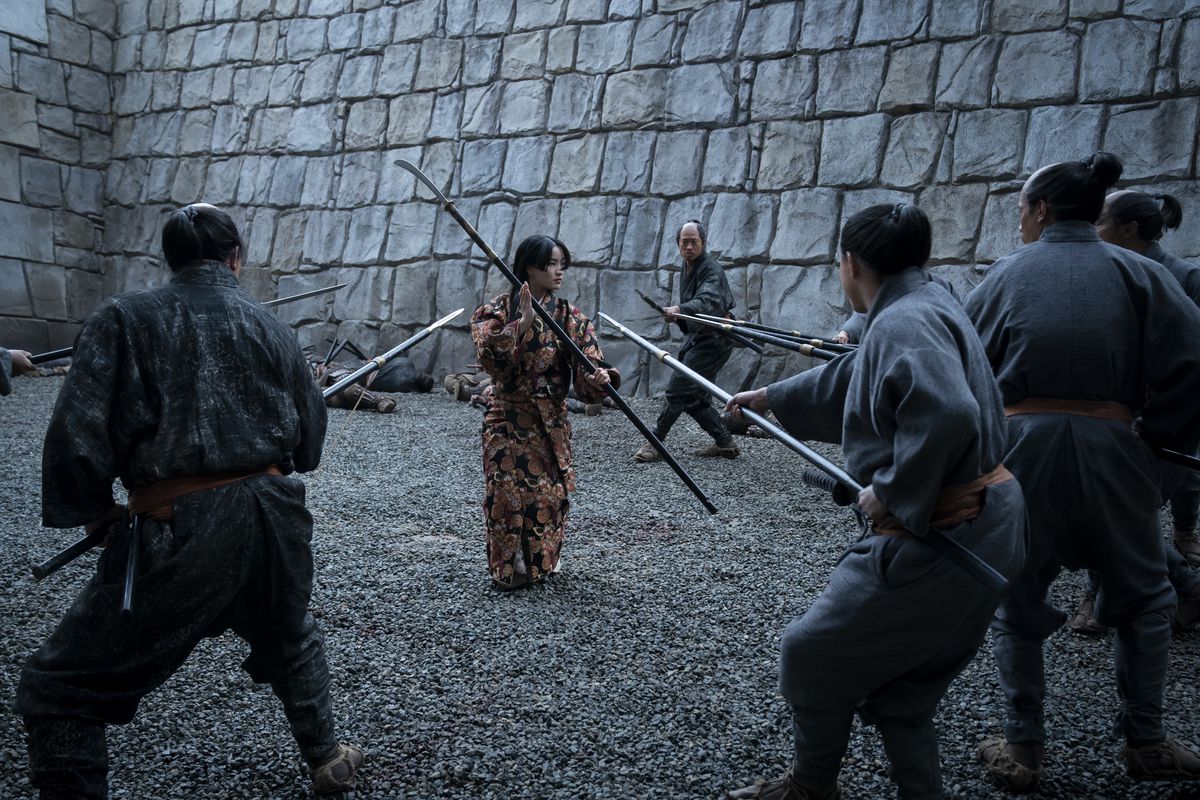 Anna Sawai håller upp en naginata medan hon är omgiven av män som svingar spjut i Shogun