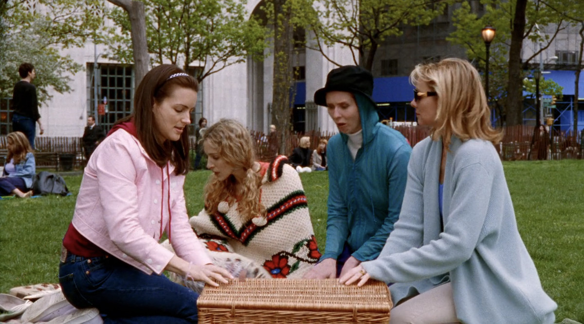 En stillbild av Sex and the City.  Carrie, Miranda, Charlotte och Samantha har picknick.  Carrie har en poncho på sig. 