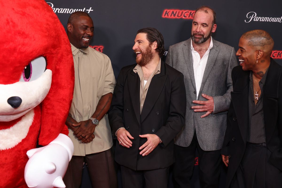 Knuckles står mörkt på en röd matta-bild med sin Knuckles-roll av Idris Elba, Adam Pally, Rory McCann och Kid Cudi medan de alla skrattar
