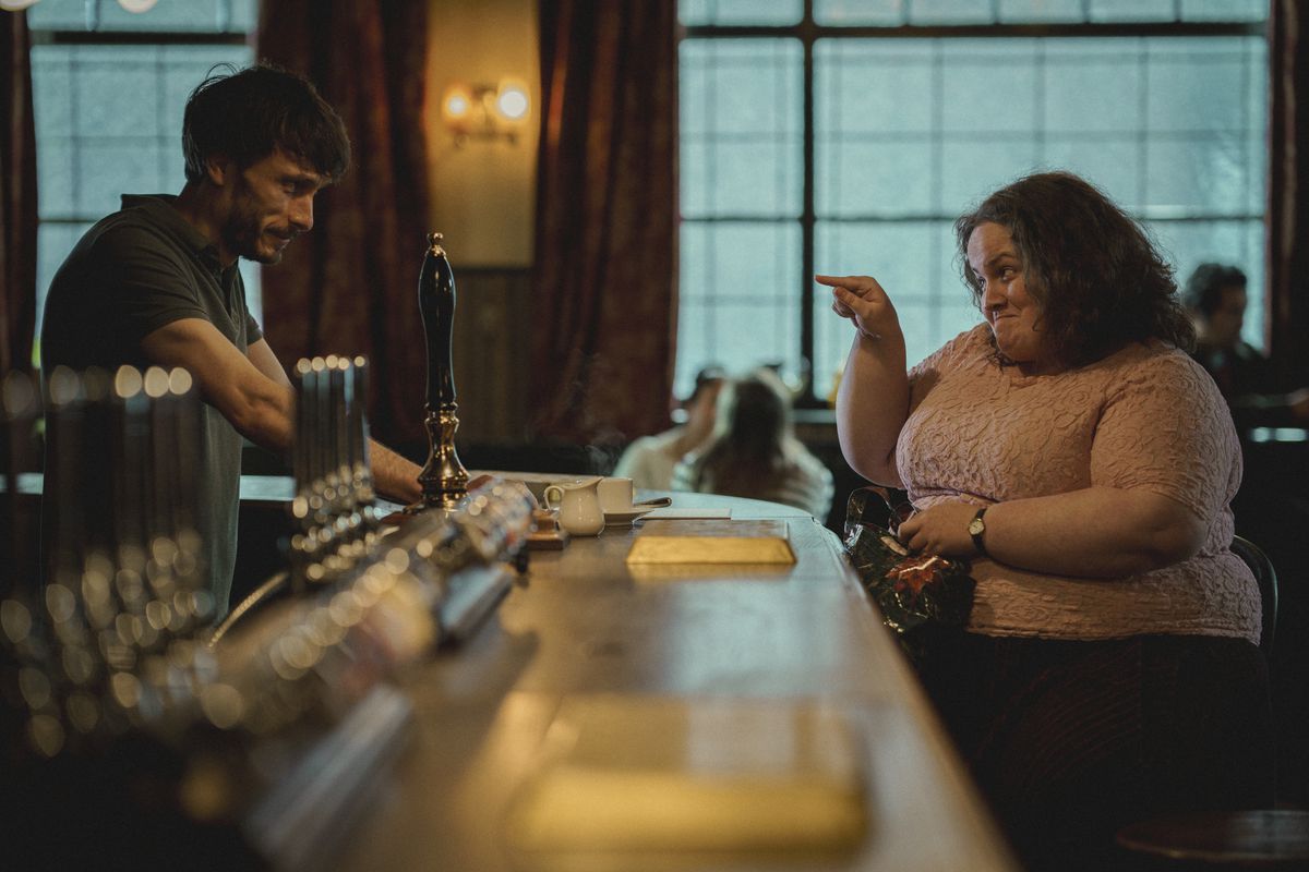 Richard Gadd och Jessica Gunning tittar på varandra över baren på en pub i Baby Reindeer.  Hon pekar på honom och ler