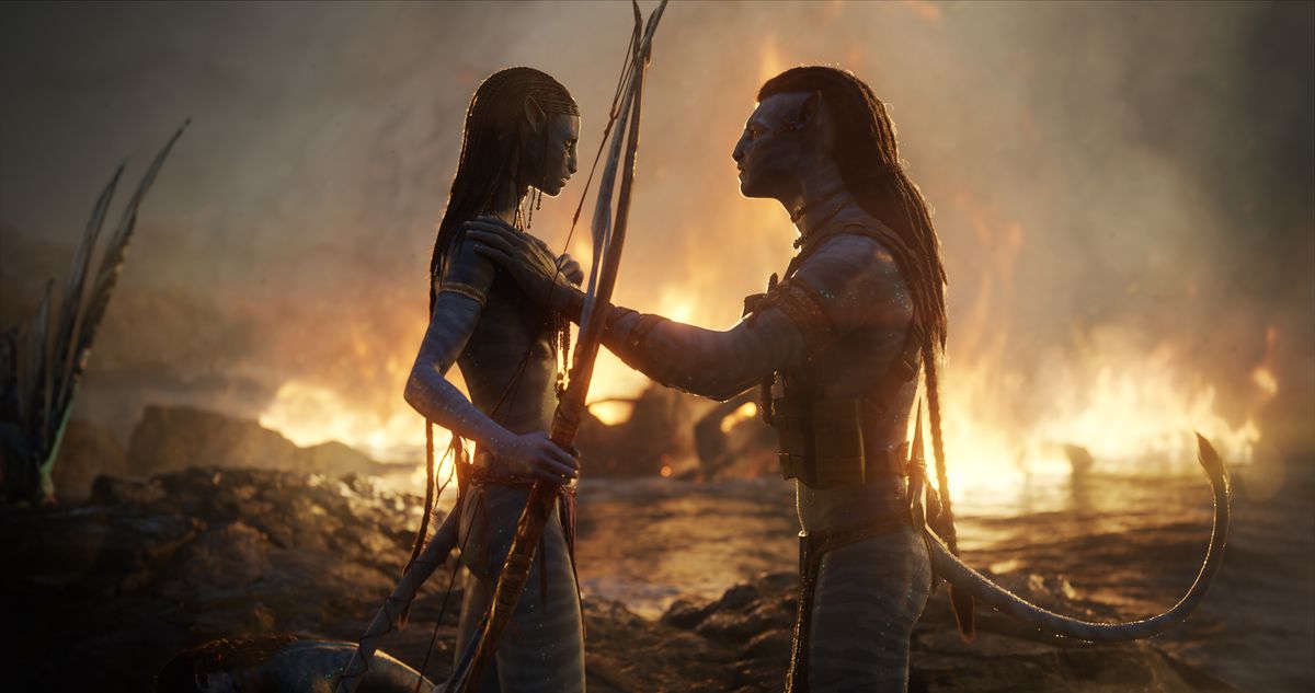 Jake Sully och Neytiri tröstar varandra efter strid, med en eld som brusar bakom dem över vattnet i Avatar: The Way of Water
