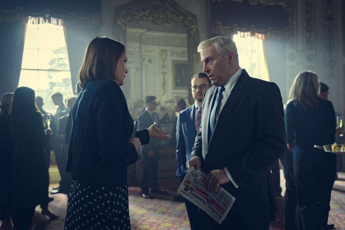 A man speaking to a man holding a newspaper with a concerned expression on his face.