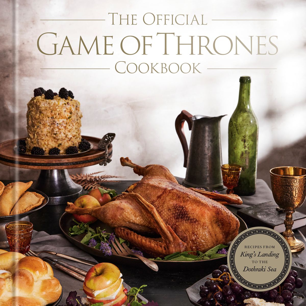 Omslaget till The Official Game of Thrones Cookbook, med olika kakor, bröd, stekt fågel och dryckeskärl i medeltida stil.