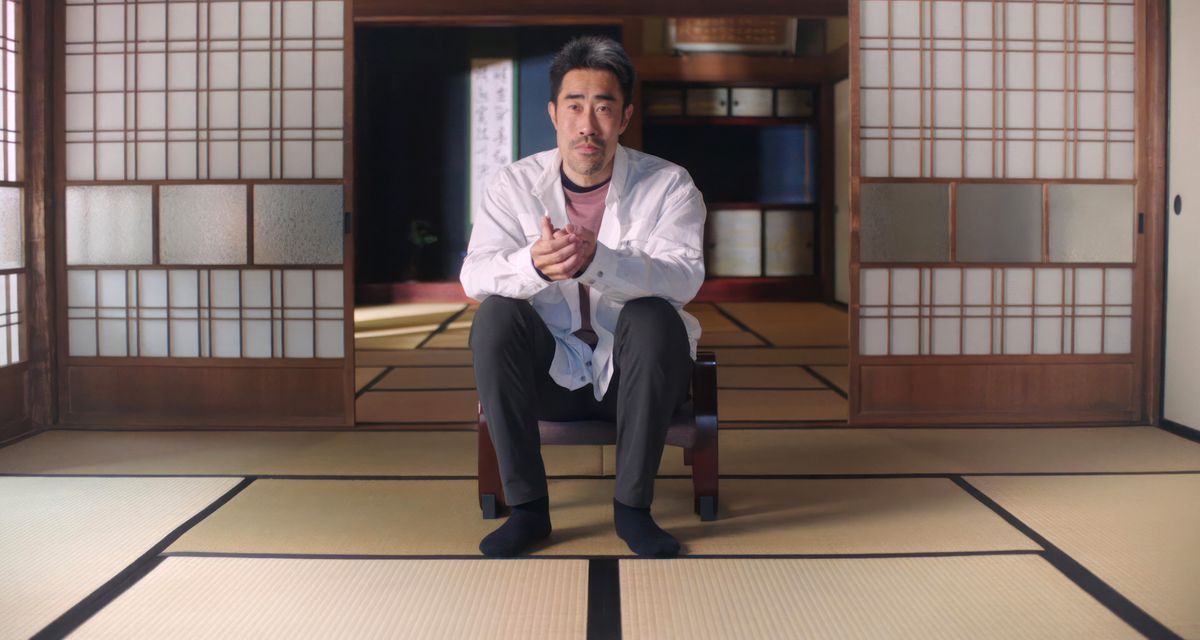 Den tävlande ämnet Nasubi i en modern intervju, sittande i ett rum med tatamigolv framför öppen shoji, med håret snyggt kortklippt