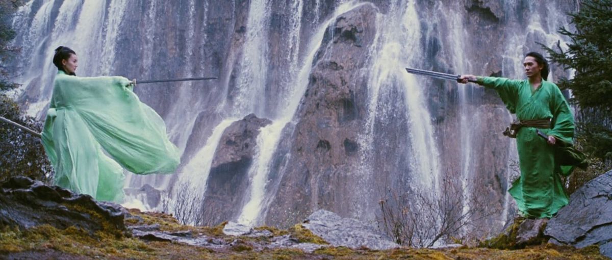 Maggie Cheung and Tony Leung wear bright green outfits and point swords at each other in front of a waterfall in Hero