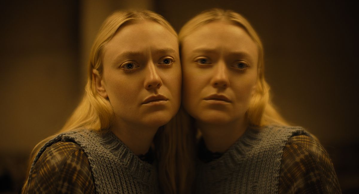 Dakota Fanning as Mina in The Watchers. She has her cheek pressed against a large mirror, creating an eerily symmetrical image. 