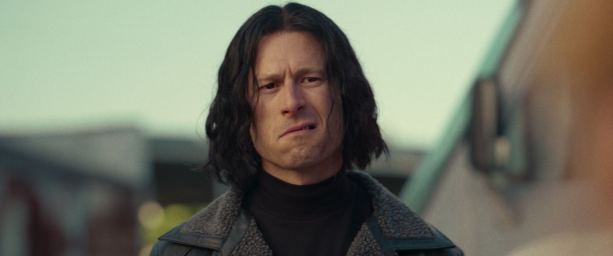 Glen Powell as Gary in Hit Man. He’s sneering badassfully while wearing a ridiculous wig. 