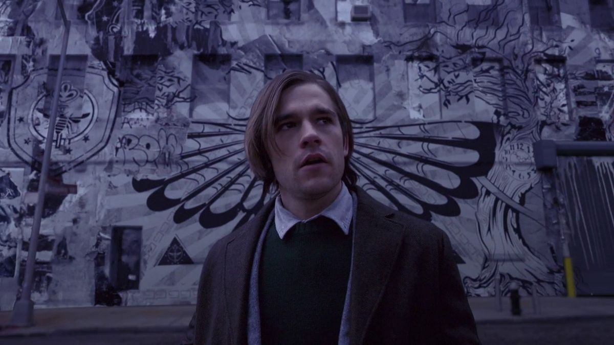 Quentin Coldwater står framför en vägg med graffiti i en scen från The Magicians.