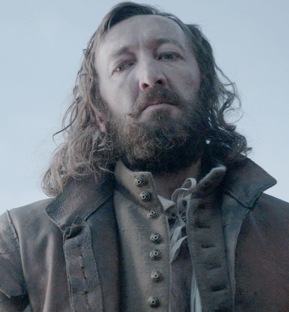 Ralph Ineson i The Witch som står i en stor rock med sitt stora skägg skymt över kameran