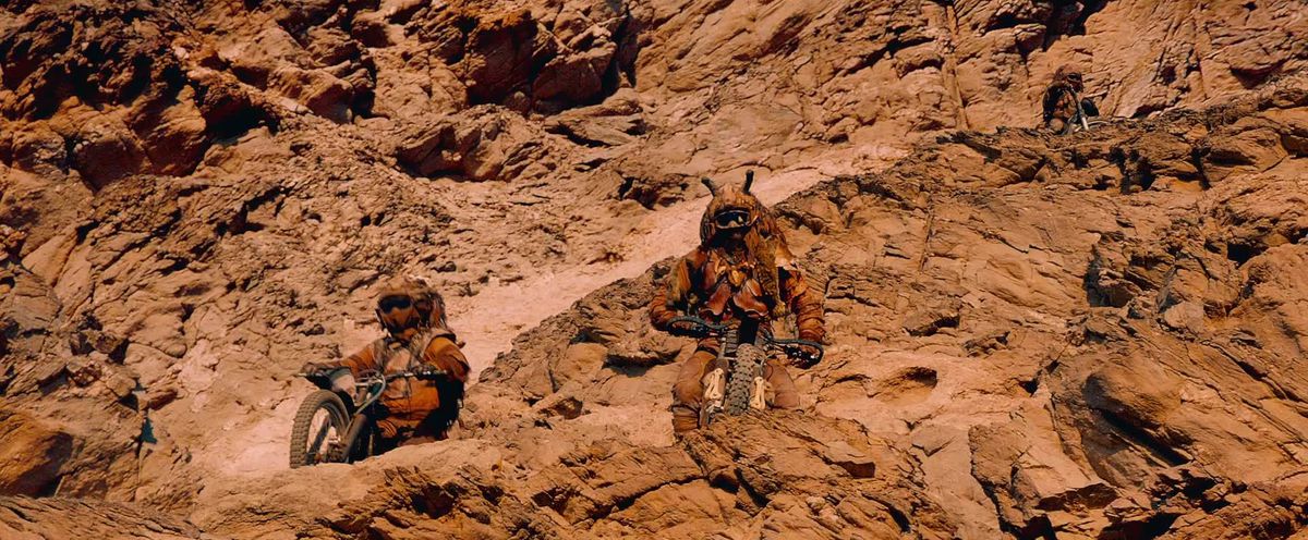 Två Rock Riders, på motorcyklar, vilar på en bergsyta och tittar över kanten i Mad Max: Fury Road