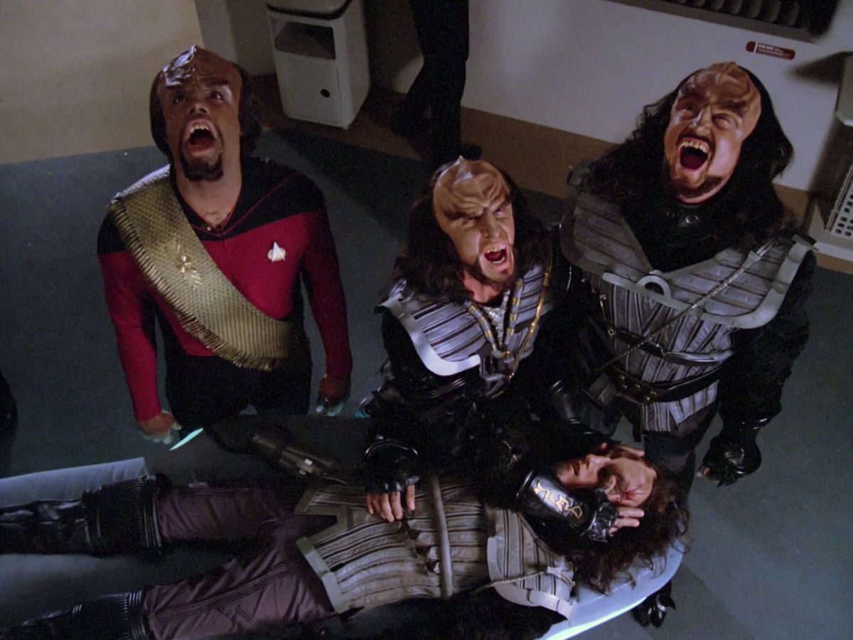 Worf och två andra klingoner skriker mot himlen, medan en av dem blundar på en fjärde, fallen klingon i Star Trek: The Next Generation