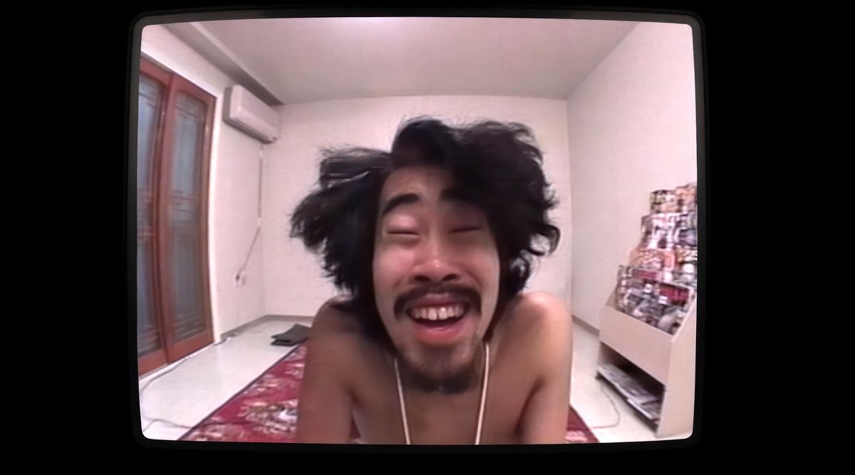 Nasubi, en japansk man med vilda, ovårdade långt hår, flinar in i kameran i en scen från Hulus dokumentär The Contestant