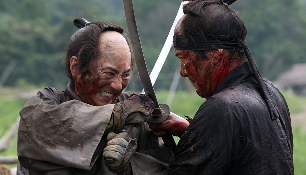 Two men with bloody faces cross swords in what looks like a desperate fight in 13 Assassins