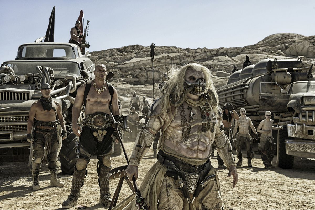 lr: Nathan Jones som Rictus Erectus och Hugh Keays-Byrne som Immortan Joe står omgivna av War Boys och enorma fordon i Mad Max: Fury Road.