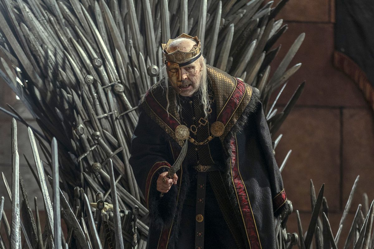 Paddy Considine som Viserys Targaryen bär en guldmask, viftar med en dolk och står framför Iron Throne på House of the Dragon
