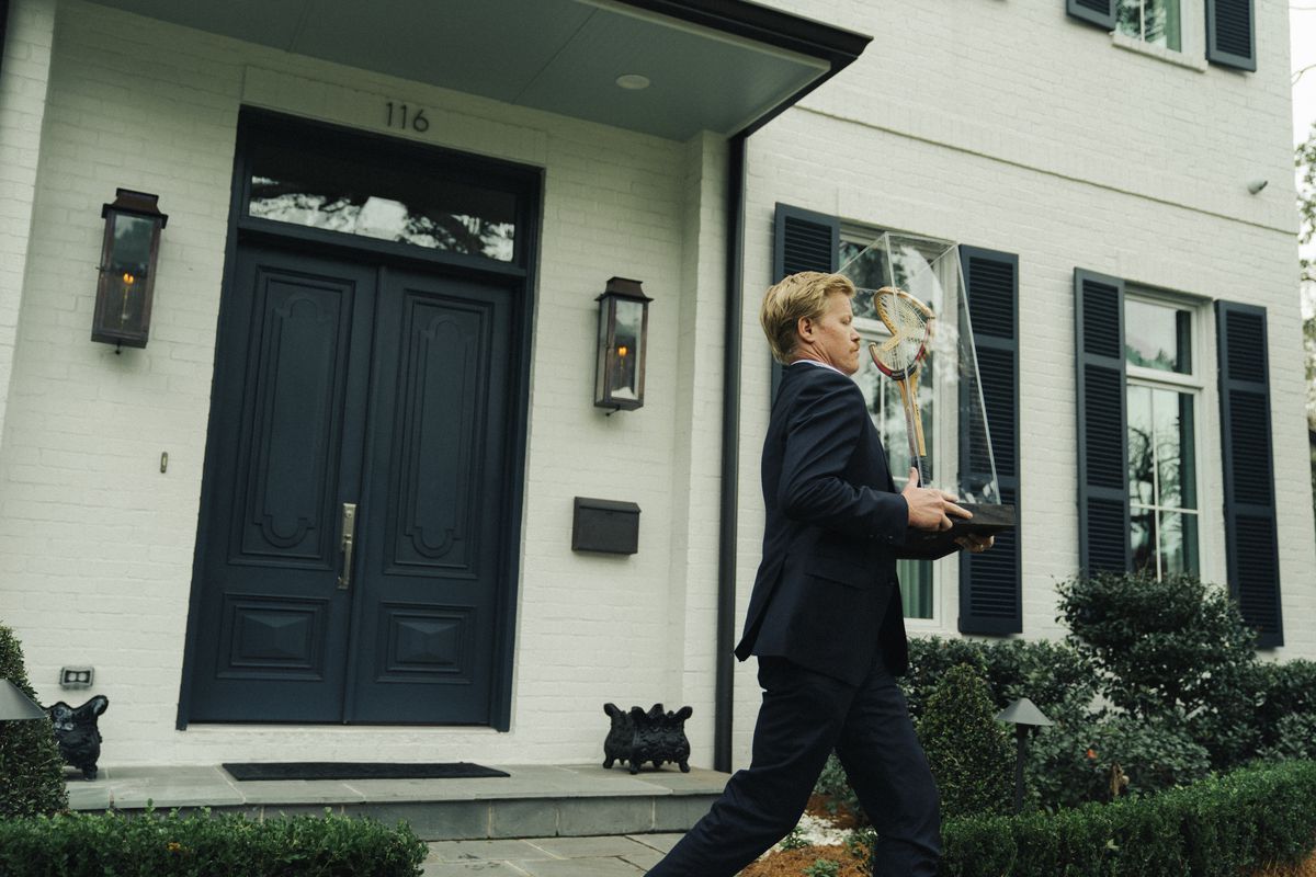 Jesse Plemons bär en trasig tennisracket i trä i en glasmonter förbi ett elegant hus i Kinds of Kindness