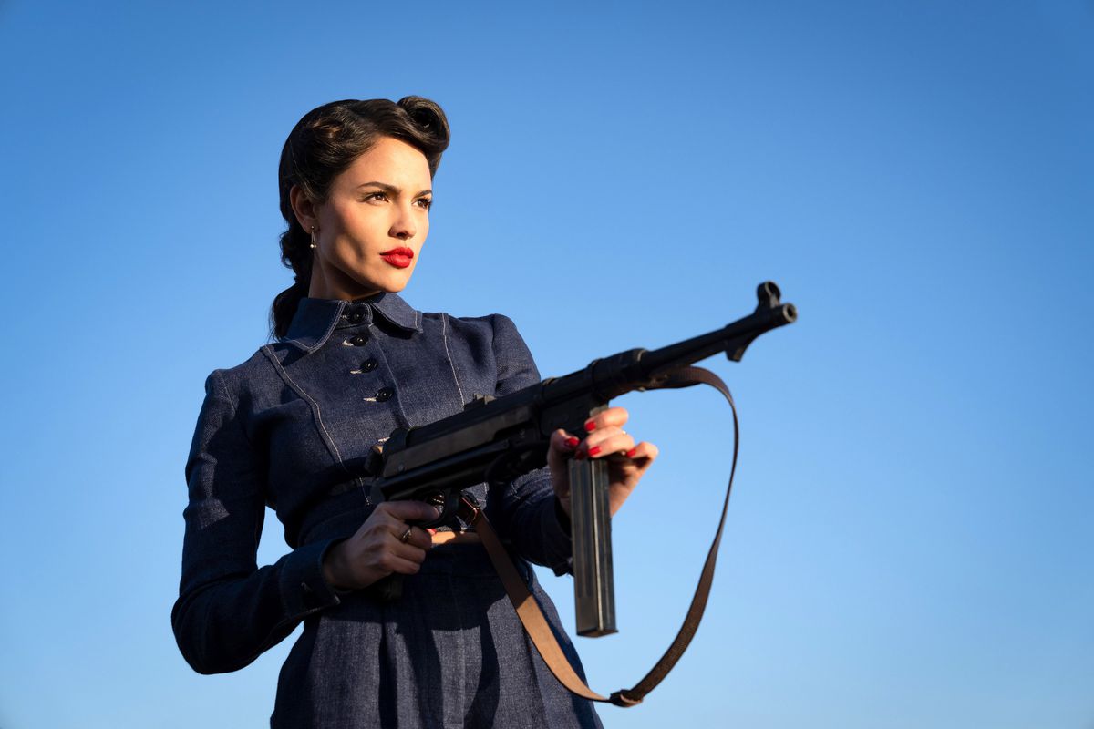 Eiza González, i en smart 1940-talsklänning och scharlakansröd läppstift, håller ett maskingevär i The Ministry of Ungentlemanly Warfare