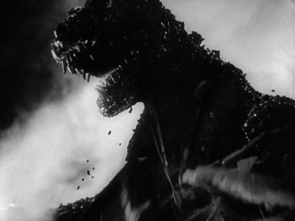 A close-up shot of a gigantic lizard-like creature baring its teeth with smoke pouring out of its mouth in Godzilla.